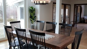 A dining area with a wooden table and black chairs, a hanging light fixture, and a potted plant.