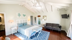 A bedroom with a bed, a sofa, a ceiling fan, and artwork on the walls.