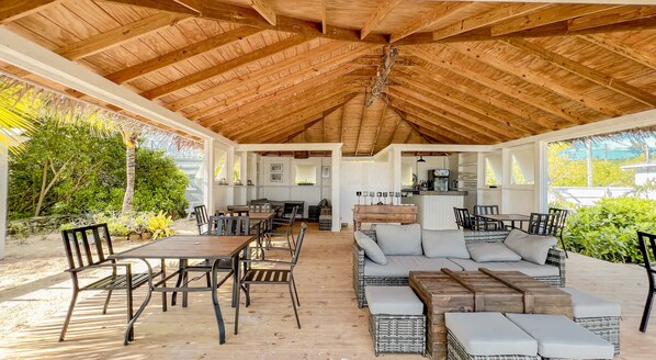 Un patio extérieur abrité, doté d’un plancher en bois et de mobilier, notamment des tables et des canapés.