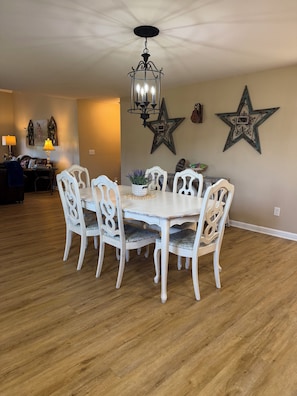 A dining area with a chandelier, white chairs, a wooden table, and decorative star wall art. - Brick Farmhouse Retreat – 7 Minutes to Red Clay State Park (Cleveland)