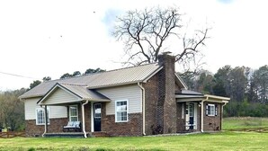 A two-story house with a brick exterior and a metal roof, featuring a front porch with a bench. - Brick Farmhouse Retreat – 7 Minutes to Red Clay State Park (Cleveland)