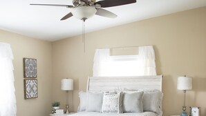 A bedroom with a bed, a ceiling fan, bedside lamps, a nightstand, and a small table with a clock. - Brick Farmhouse Retreat – 7 Minutes to Red Clay State Park (Cleveland)