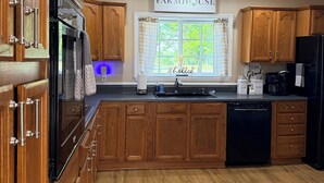 A kitchen with wooden cabinets, a black refrigerator, a dishwasher, and a window with a view of greenery. - Brick Farmhouse Retreat – 7 Minutes to Red Clay State Park (Cleveland)