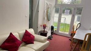 A living room with a beige sofa, red cushions, a small table with a vase, and a glass door leading outside. - Luxurious room nearby Copenhagen central (Rødovre)