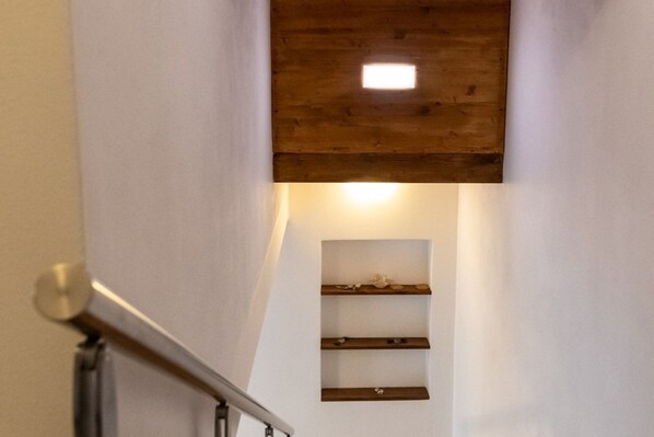 A staircase with a wooden ceiling and a small shelf with decorative items.
