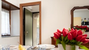Un comedor con una mesa preparada para dos personas, un jarrón de tulipanes rojos y una pera sobre la mesa.