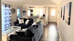 A modern living room with a sofa, a glass coffee table, and a kitchen in the background. - Cape Gem in New Seabury resort & near the beach. (Mashpee)