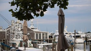 A marina with boats docked, a building with a white facade, and a tree overhead. - Cape Gem in New Seabury resort & near the beach. (Mashpee)
