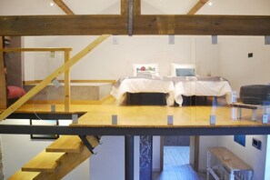 Une chambre de style « loft », avec un plafond haut, des poutres apparentes et un escalier menant à un niveau supérieur.