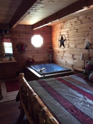 Relax in a cabin-style room with a hot tub, comfortable bed, and a window offering a view of the outdoors.