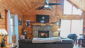 A cabin interior with a fireplace, a ceiling fan, a television, and a sofa. - Bear Necessities: peaceful, With/romantic hot tub. (Sevierville)