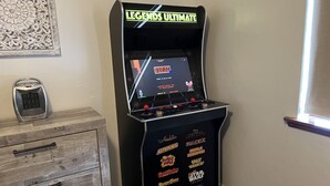 En spillehal med et udvalg af klassiske arkadespil, herunder 'Fix It Felix' og 'Tetris', samt en dekorativ genstand til venstre.