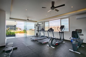 A modern gym with treadmills, elliptical machines, and a rowing machine, large windows with a city view, and a ceiling fan. - Top-Floor Penthouse · Walk to Beach · King Bed (Puerto Vallarta)