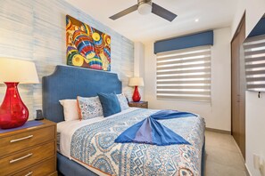 A bedroom with a bed, two nightstands, a ceiling fan, a window with blinds, and a colorful painting above the bed. - Top-Floor Penthouse · Walk to Beach · King Bed (Puerto Vallarta)