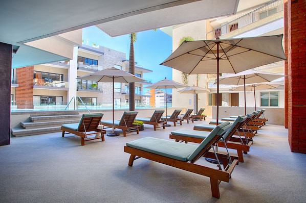 A rooftop lounge area with sun loungers and umbrellas, overlooking a cityscape. - Top-Floor Penthouse · Walk to Beach · King Bed (Puerto Vallarta)