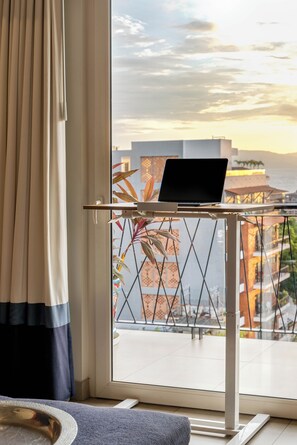 A laptop on a balcony table with a view of buildings and a sunset. - Top-Floor Penthouse · Walk to Beach · King Bed (Puerto Vallarta)