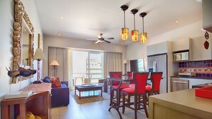 Ein modernes Hotelzimmer mit Essbereich, einem Balkon mit Vorhängen, einem Deckenventilator und einer Küche mit Kühlschrank und Mikrowelle.