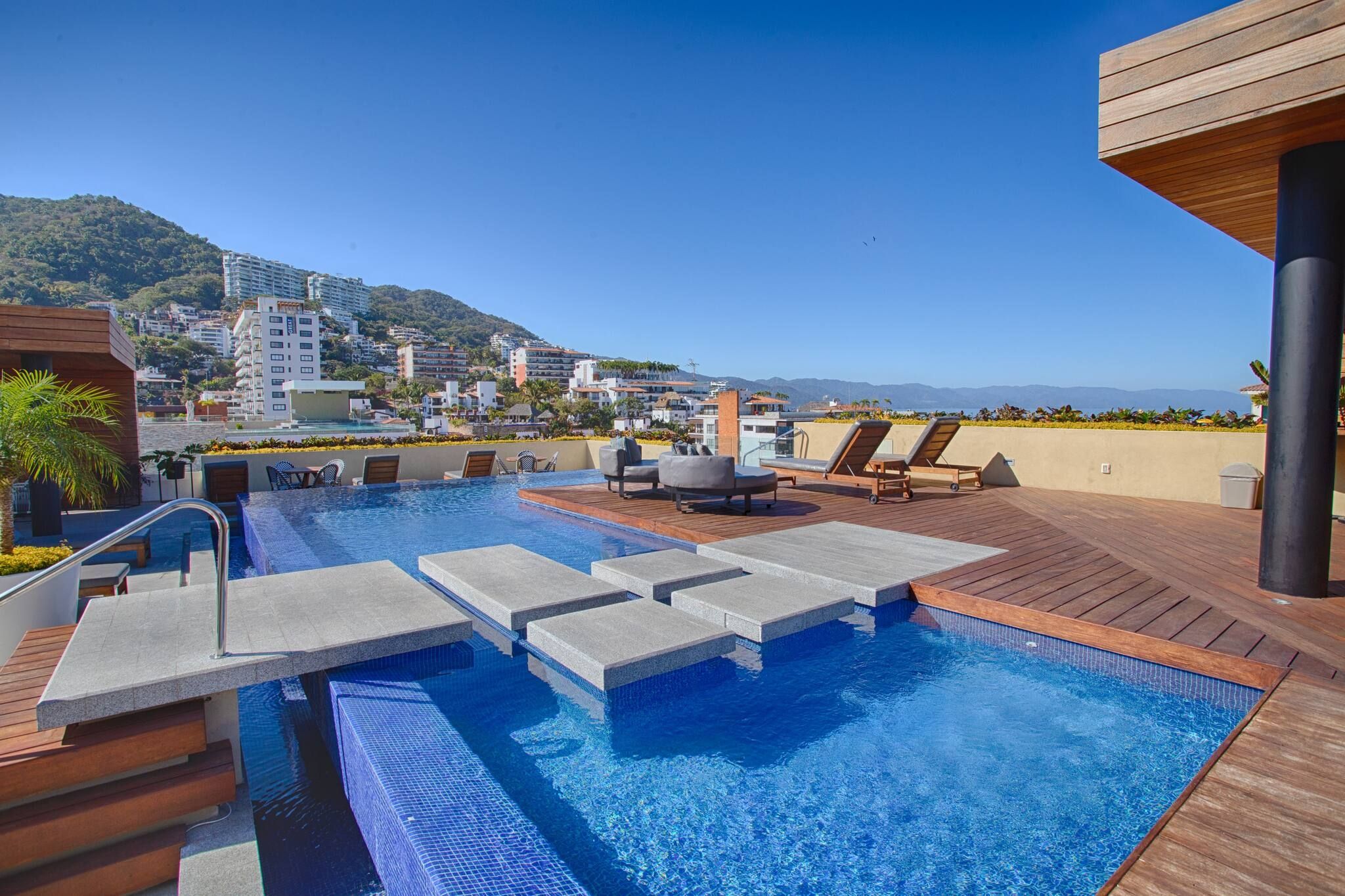 Una piscina en la azotea con sillones de descanso y vistas a un paisaje urbano.