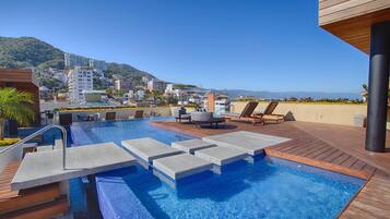 Una piscina en la azotea con sillones de descanso y vistas a un paisaje urbano.