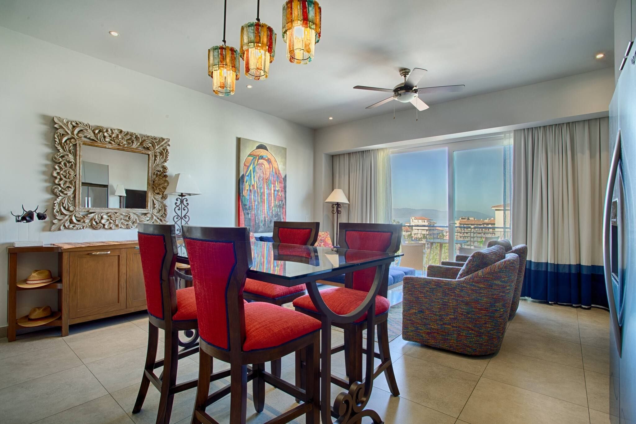 Habitación de hotel con zona de comedor, un amplio ventanal con vistas y un ventilador de techo.
