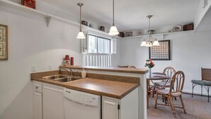 Una cocina con encimeras de granito, armarios blancos, lavavajillas integrado e iluminación colgante.
