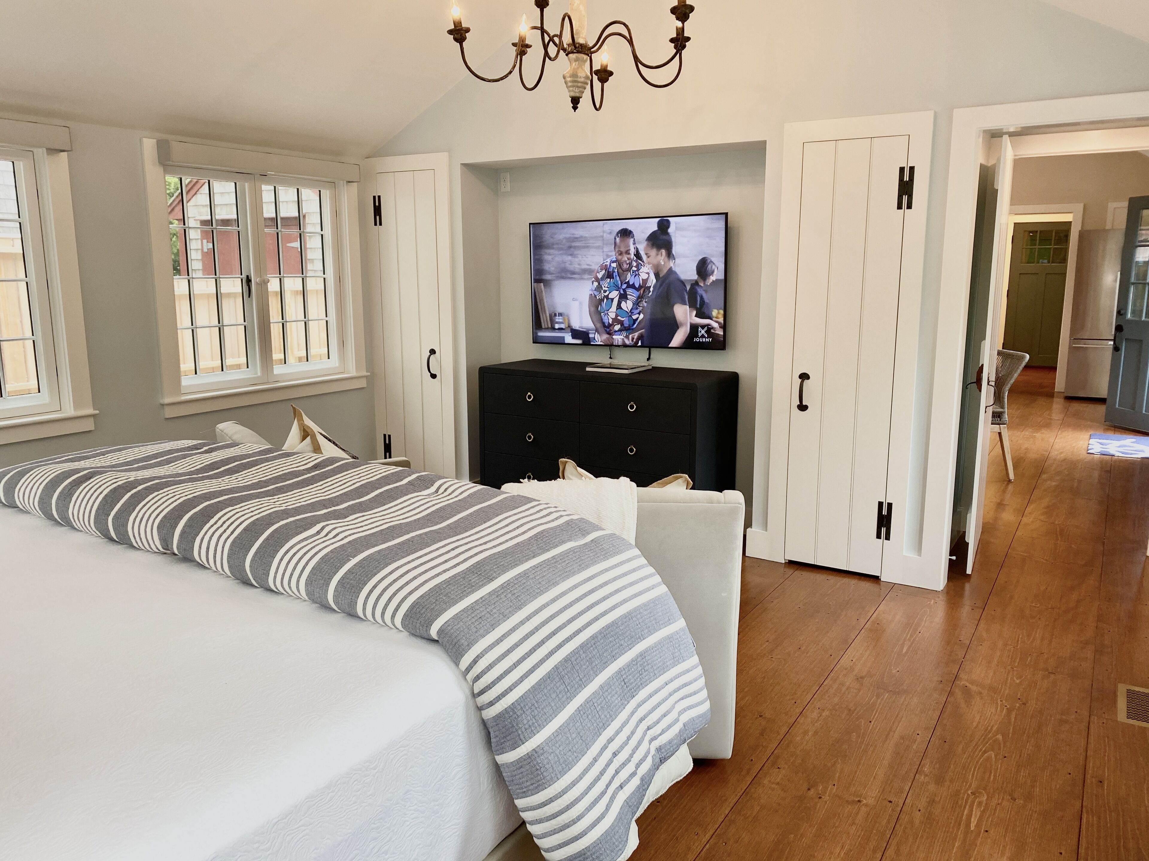 A bedroom with a large bed, a TV on a black cabinet, and a chandelier.