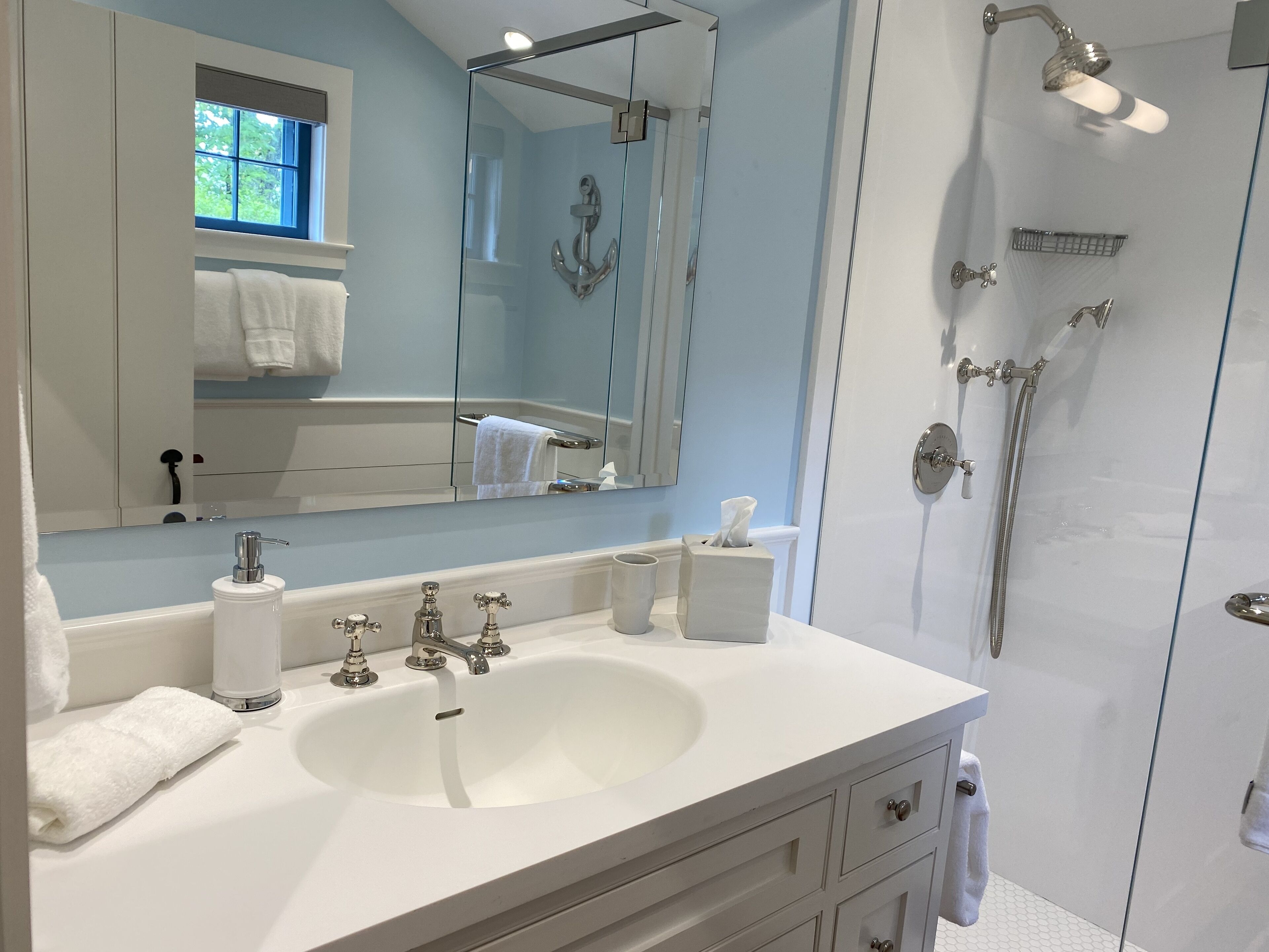 Une salle de bain avec un lavabo blanc, un miroir et une cabine de douche en verre.