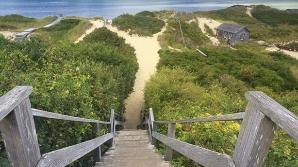 A wooden staircase leading to a beach area with a small building and a view of the ocean.