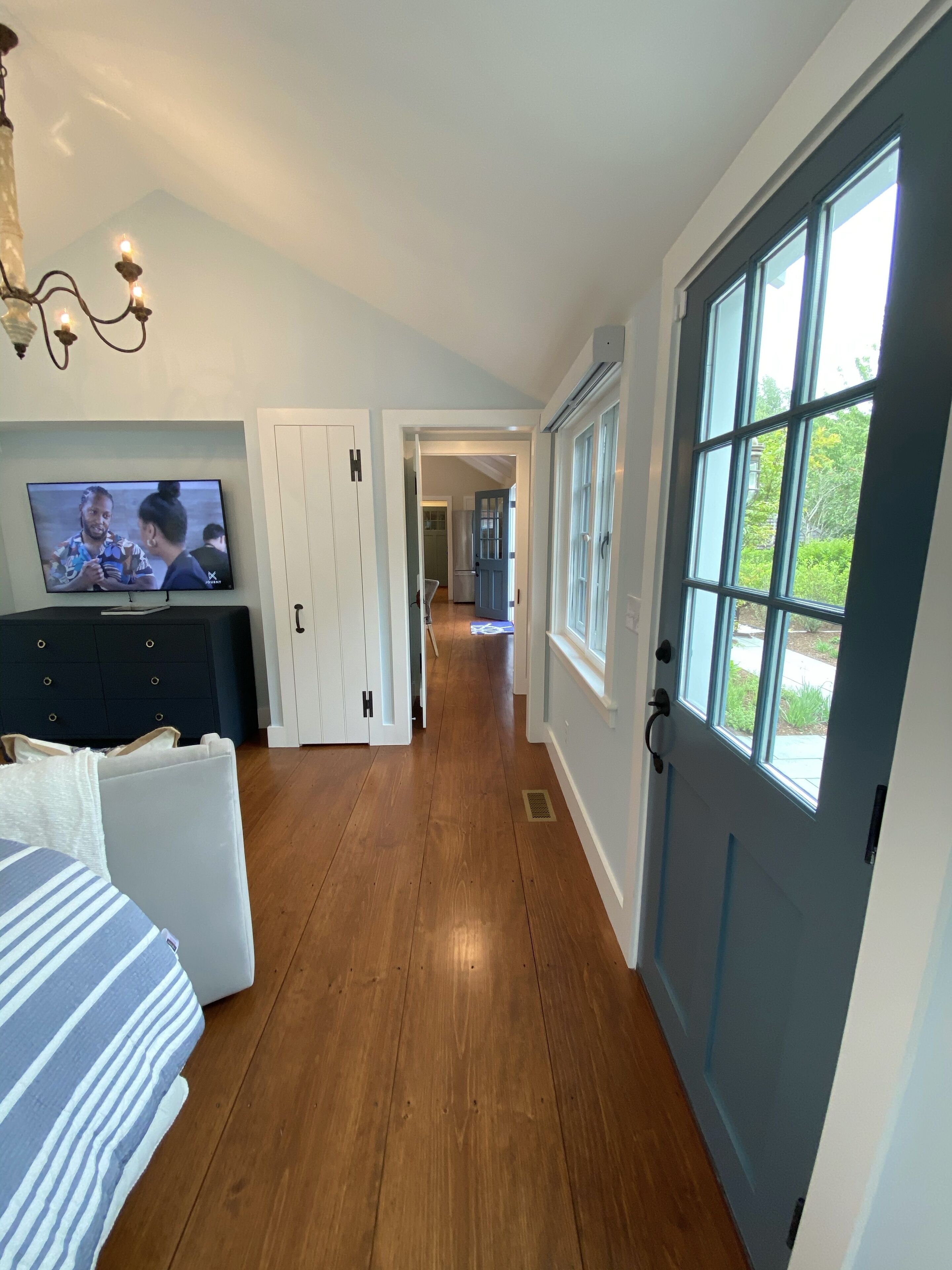 A hallway with a bed, a TV, and a door leading to a kitchen.