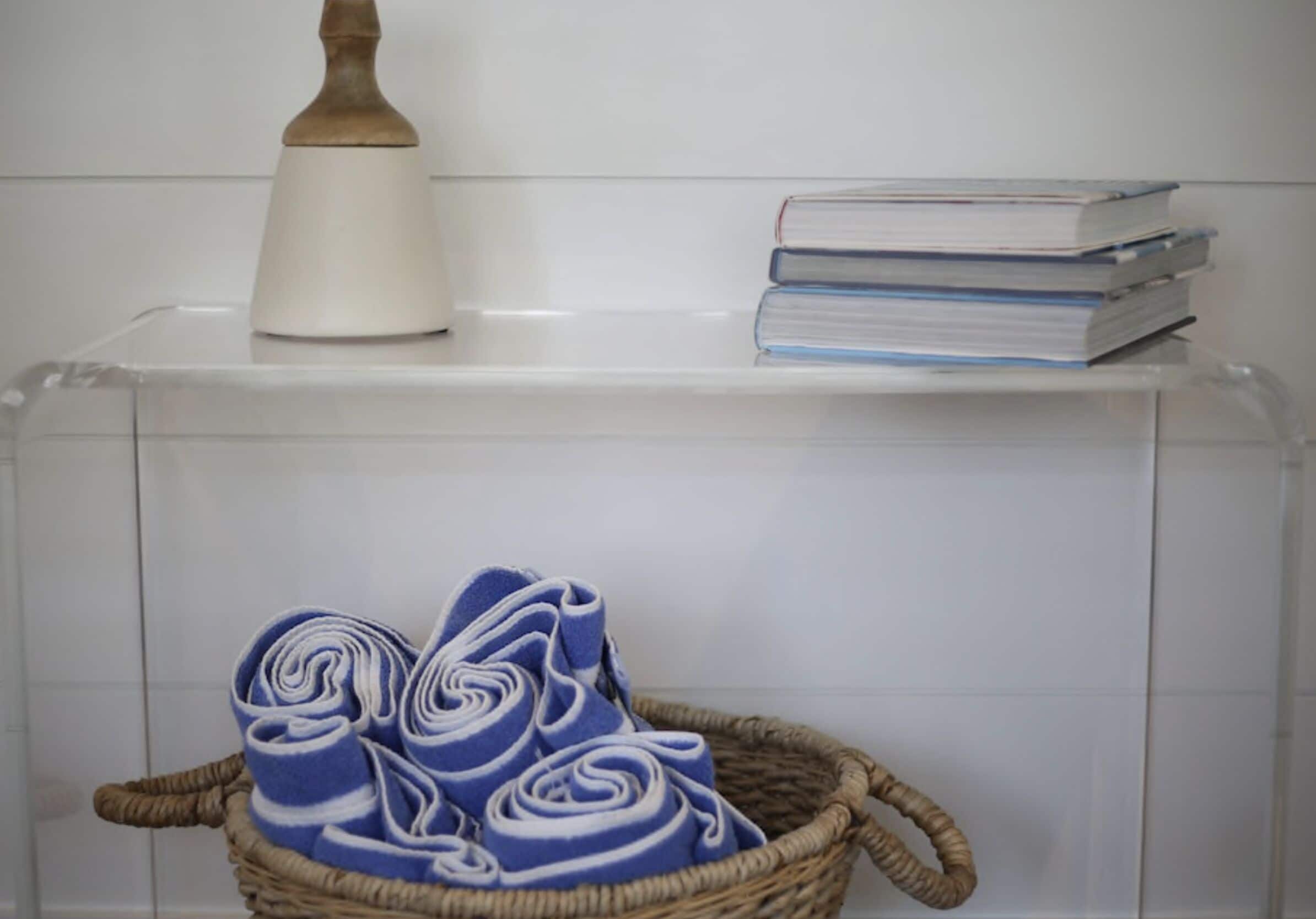 Un baño con cabina de ducha transparente, un tapete de baño de madera y una pila de libros en un estante.