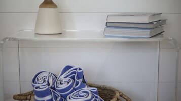 Un baño con cabina de ducha transparente, un tapete de baño de madera y una pila de libros en un estante.