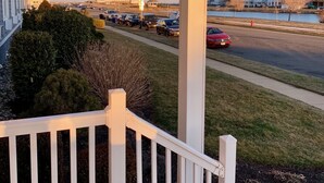 A covered porch with a white railing overlooking a parking lot and a body of water.