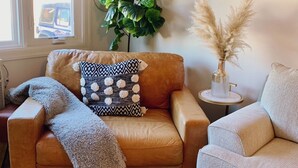 A living room with a brown leather sofa, a patterned throw blanket, and a potted plant.