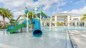 A water park area with a blue slide, a pool, and a building with a covered patio. - Lux Disney Villa | Pool, Theater/games | Sleeps 22 (Kissimmee)