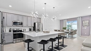 A modern kitchen with stainless steel appliances, a central island with bar stools, and pendant lighting. - Lux Disney Villa | Pool, Theater/games | Sleeps 22 (Kissimmee)