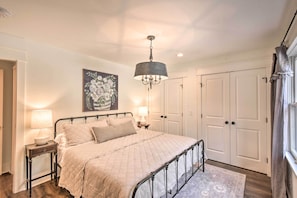 Classic bedroom with a large bed, bedside tables, and a chandelier, featuring a floral painting and double doors.