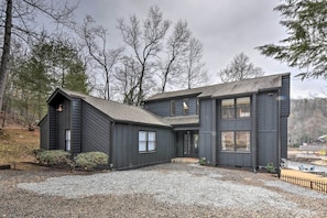 Symmetrical two-story house with a central entrance and two wings, set amidst mature trees and a gravel driveway.