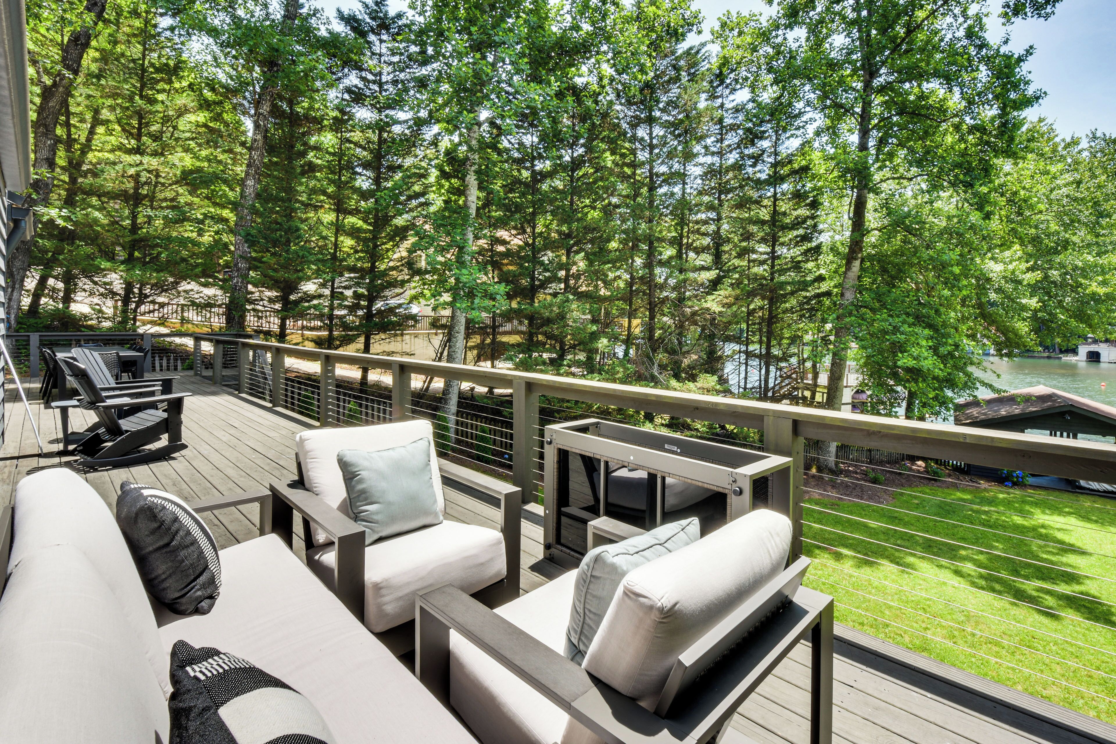 Une terrasse dotée de mobilier d’extérieur, d’une rambarde et offrant une vue sur un lac et des arbres.