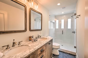 Features a marble vanity with dual sinks and a large mirror, alongside a glass-enclosed shower with a handheld showerhead.