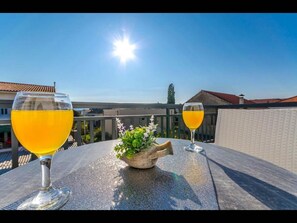 Une terrasse avec deux verres d’une boisson jaune, une petite plante et un ciel bleu clair, avec le soleil.