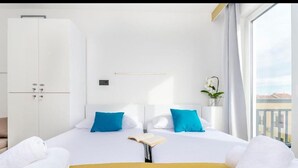 A hotel room with a bed, pillows, a bedside table with a book, a wardrobe, and a window with a view. - All Saints Suites B&b Kastela - Double Room (Kaštel Štafilić)