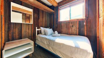 Una habitación de madera con una cama, una mesita y una ventana.
