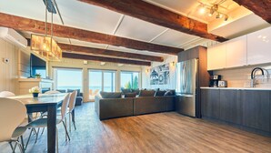 A modern kitchen with wooden beams, a dining area with a large table and chairs, and a view of the outdoors.