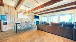 A spacious living area with a wooden floor, a sofa, a dining table with chairs, and a coffee machine.
