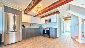 A modern kitchen with stainless steel appliances, wooden flooring, and exposed wooden beams.
