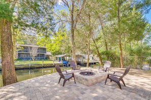 Relax by the fire pit in a serene outdoor space surrounded by lush greenery and a tranquil body of water.