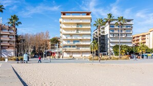 A beachfront hotel with multiple floors, a sandy beach in the foreground, and palm trees.