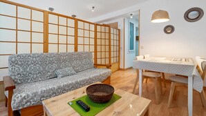 A living room with a sofa, a dining table, and a small table with a remote control.