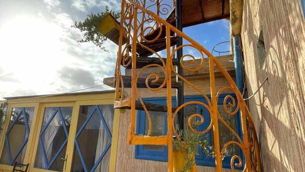 Edifici groc amb una escala espiraltra i una finestra amb marc blau.