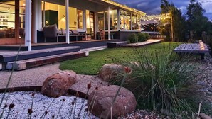 A house with a covered porch, outdoor seating, and a well-maintained garden. - Reimagined Designer Lakehouse in Prime Location (Burrill Lake)